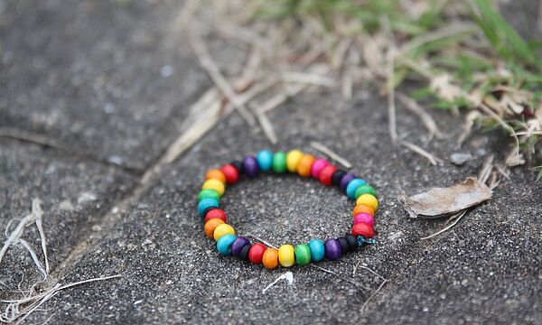 Ein Armband mit bunten Perlen liegt auf grauen Pflastersteinen